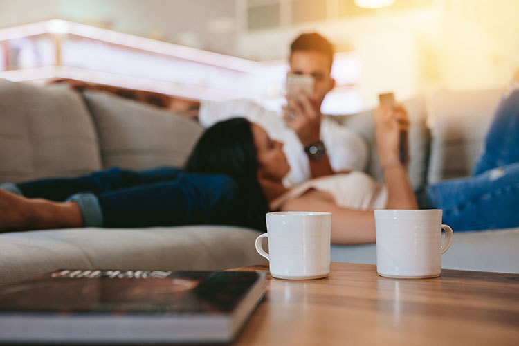 Couple lying down on couch with their phones